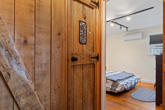 room details with a wall unit AC, wood finished floors, baseboards, and track lighting