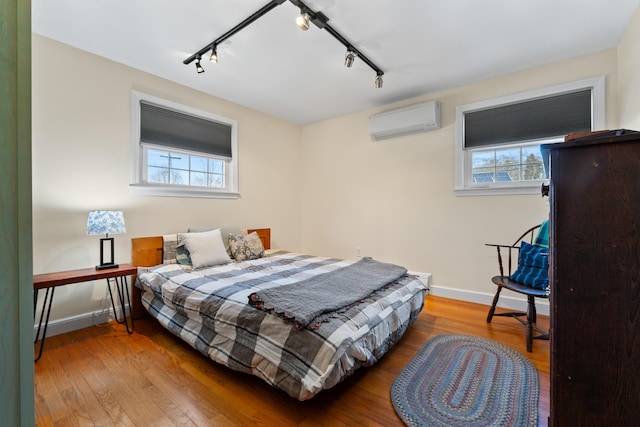 bedroom with an AC wall unit, multiple windows, wood finished floors, and baseboards