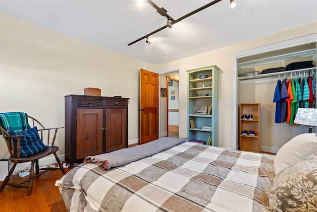 bedroom with dark wood finished floors, rail lighting, baseboards, and a closet