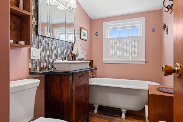 full bath featuring vanity, a freestanding tub, toilet, and backsplash