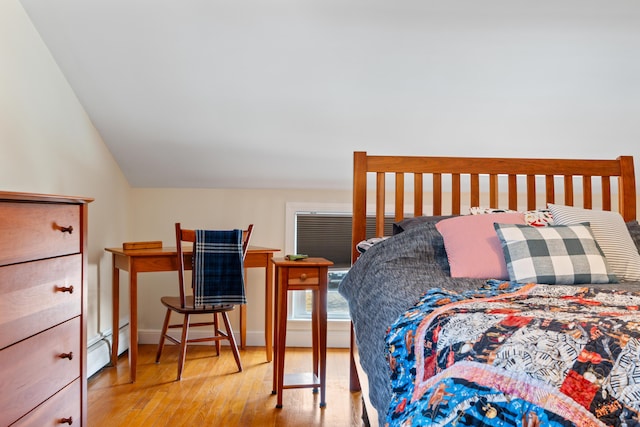 bedroom featuring a baseboard heating unit, lofted ceiling, and wood finished floors