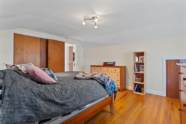 bedroom featuring light wood finished floors, baseboards, and vaulted ceiling