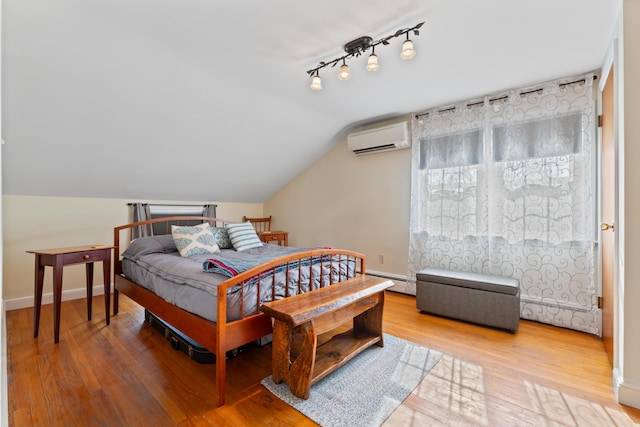 bedroom featuring an AC wall unit, track lighting, wood finished floors, baseboards, and vaulted ceiling