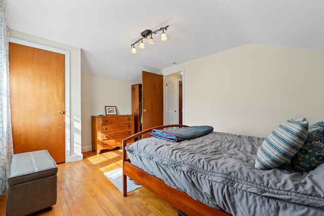 bedroom featuring lofted ceiling, baseboards, and light wood finished floors