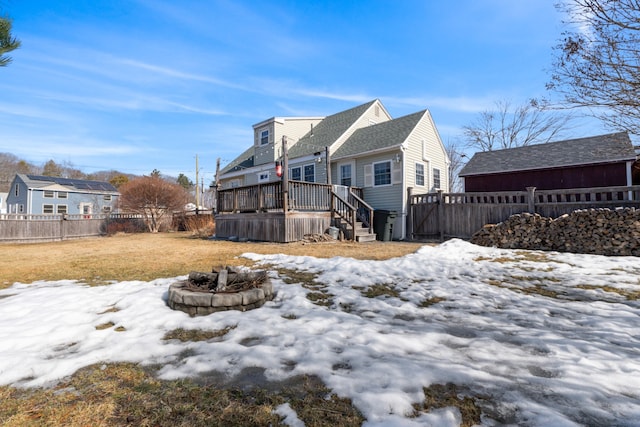 snow covered back of property with a deck, fence, and a fire pit