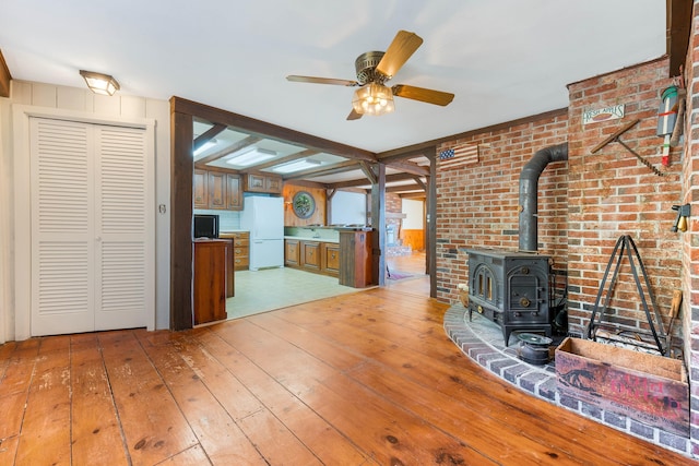 44 Periwinkle Ln, Phippsburg, ME 04562 - unfurnished living room with light wood-style flooring, brick wall, a wood stove, and ceiling fan