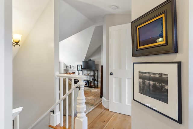 hall featuring vaulted ceiling, an upstairs landing, and light wood-style floors