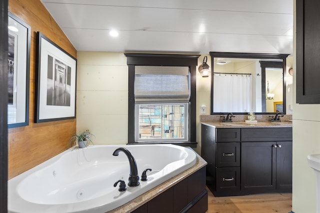 bathroom featuring double vanity, a jetted tub, wood finished floors, and a sink