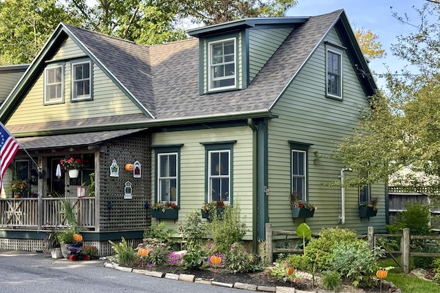 view of front facade with a porch, roof with shingles, and fence