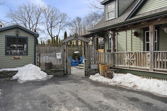 view of side of home featuring covered porch, roof with shingles, and fence