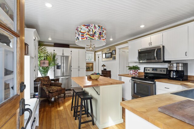 kitchen with stainless steel appliances, light wood-style floors, white cabinetry, crown molding, and butcher block counters