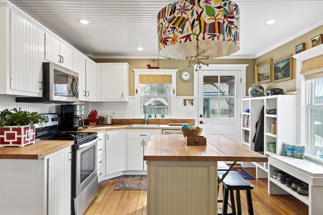 kitchen featuring wooden counters, ornamental molding, plenty of natural light, stainless steel appliances, and a sink