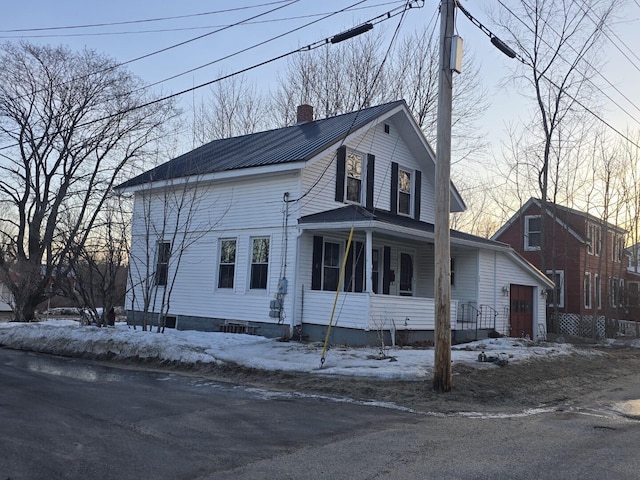 view of snow covered exterior featuring covered porch and a chimney