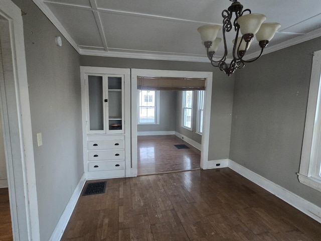 unfurnished dining area featuring visible vents, dark wood-type flooring, baseboards, ornamental molding, and a notable chandelier