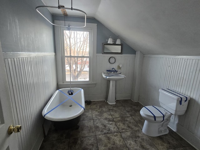 bathroom with tile patterned flooring, toilet, a freestanding bath, vaulted ceiling, and wainscoting