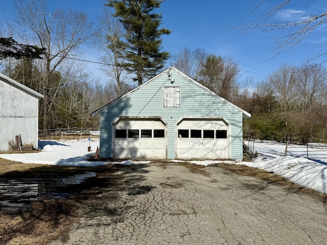 snow covered garage featuring a detached garage and fence