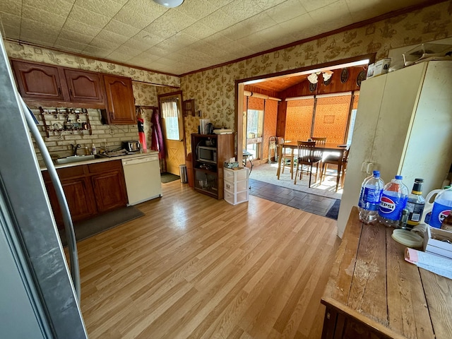 kitchen featuring wallpapered walls, light wood-style flooring, white dishwasher, a sink, and light countertops