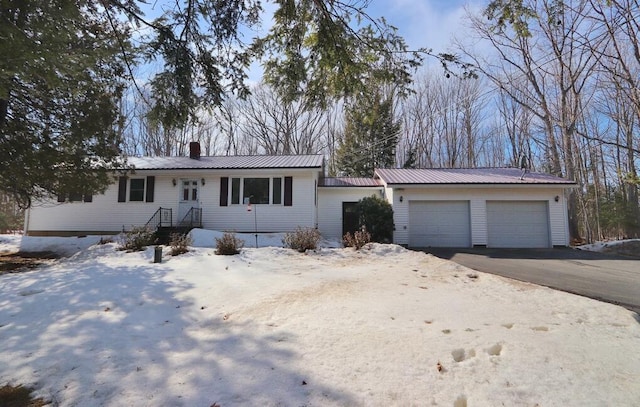 ranch-style home with a chimney, metal roof, aphalt driveway, and a garage