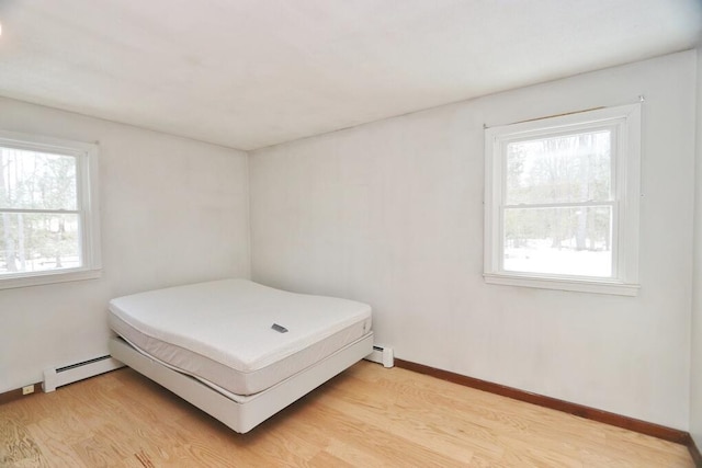 bedroom featuring a baseboard heating unit, baseboards, and light wood-type flooring