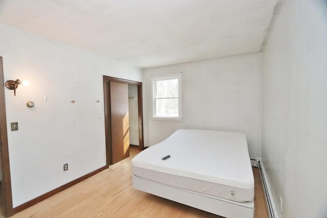 bedroom featuring light wood finished floors, a closet, a baseboard heating unit, and baseboards