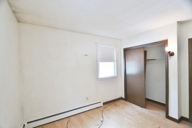 unfurnished bedroom featuring a closet, light wood finished floors, a baseboard heating unit, and baseboards