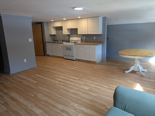 kitchen featuring light wood-type flooring, white range with gas cooktop, a sink, white cabinetry, and recessed lighting