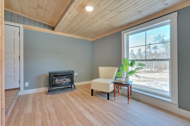 sitting room with wooden ceiling, a wood stove, baseboards, and wood finished floors