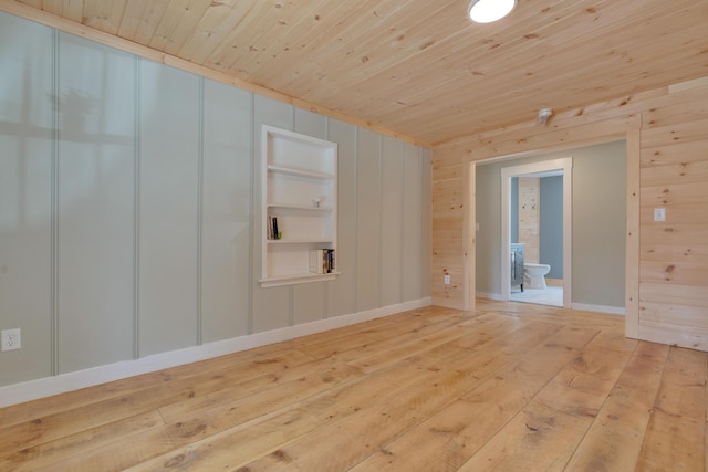 unfurnished room with wooden walls, wooden ceiling, light wood-type flooring, and built in shelves