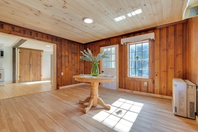 unfurnished dining area featuring light wood-type flooring, heating unit, wood walls, wooden ceiling, and baseboards