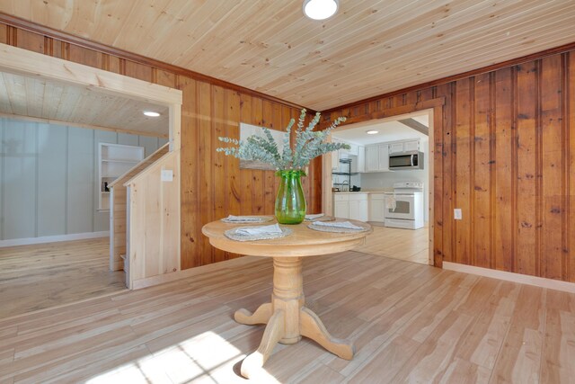 unfurnished dining area with wooden walls, light wood-style floors, baseboards, wood ceiling, and stairs