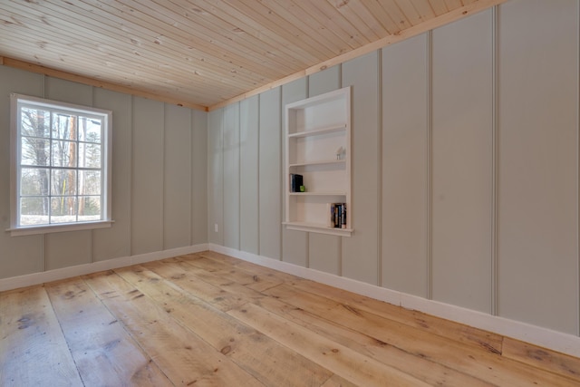 empty room featuring light wood-type flooring, built in shelves, wood ceiling, and a decorative wall