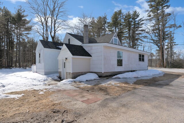 snow covered property with a chimney and a shingled roof