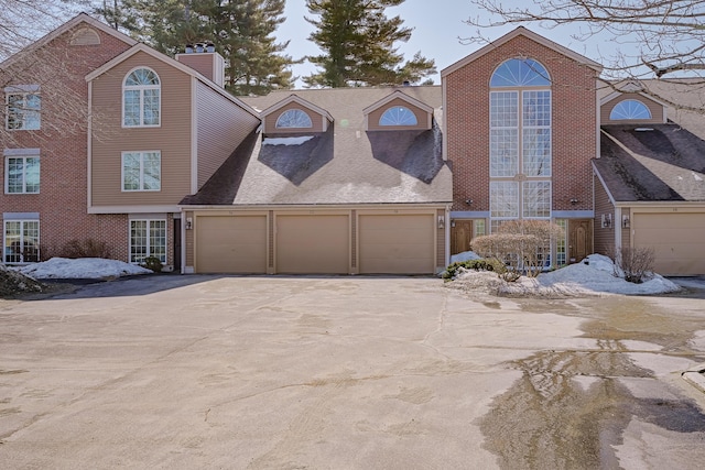 view of front of home with brick siding, driveway, a garage, and roof with shingles