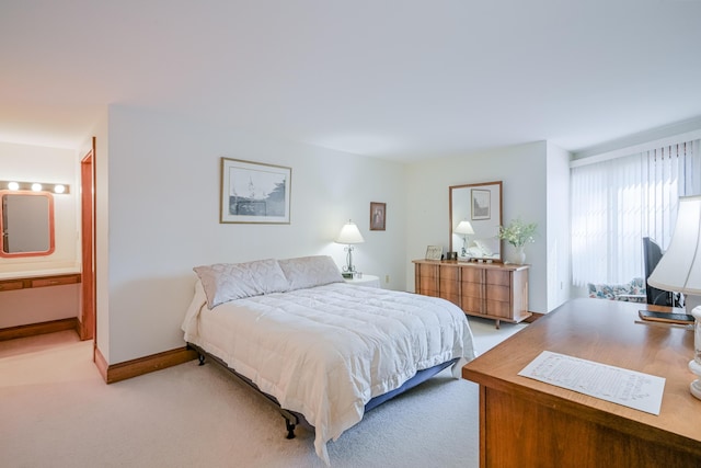 bedroom with baseboards, light carpet, and ensuite bathroom