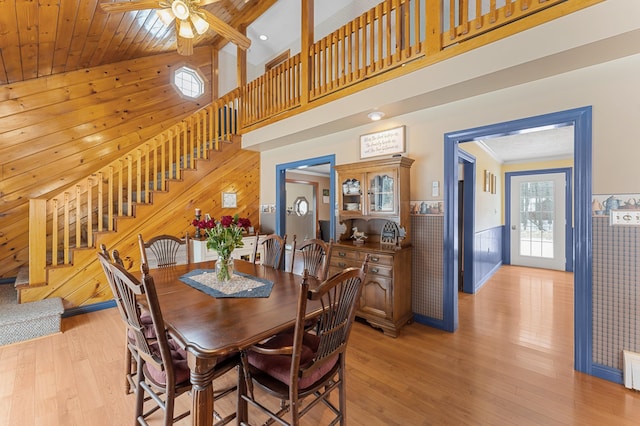 dining space with light wood-type flooring, a wainscoted wall, wooden walls, a high ceiling, and stairs