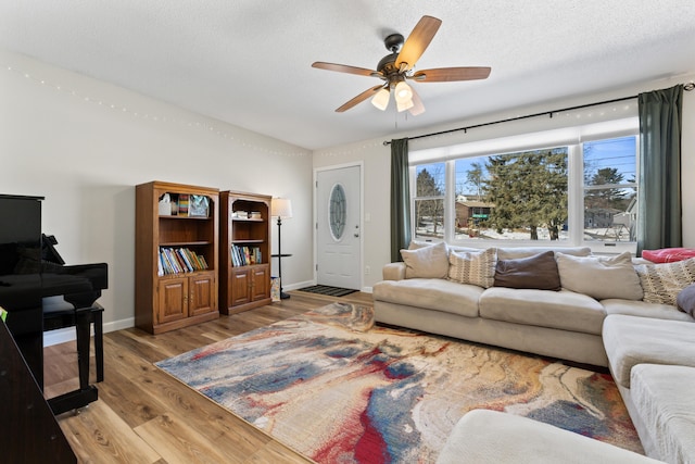 living area with baseboards, a textured ceiling, light wood-style floors, and a ceiling fan