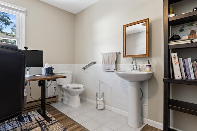 half bath with tile patterned flooring, a baseboard heating unit, toilet, wainscoting, and tile walls