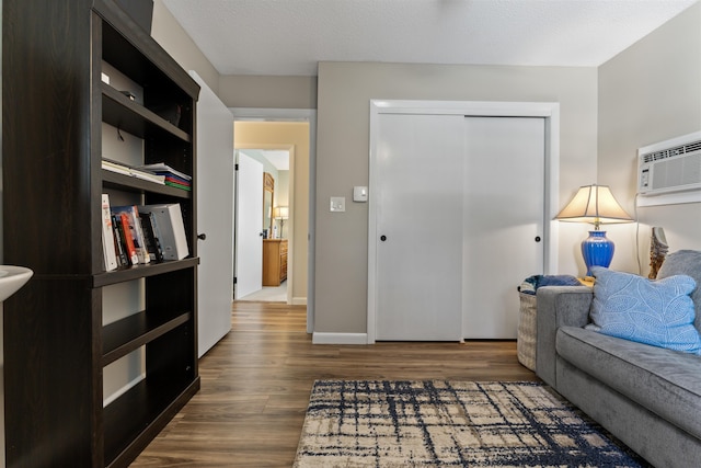 interior space with a textured ceiling, an AC wall unit, baseboards, and wood finished floors