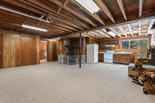 basement featuring light colored carpet, wood walls, freestanding refrigerator, a wood stove, and a sink