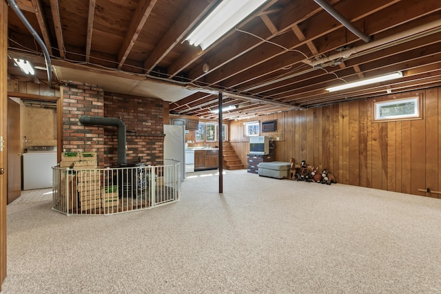 below grade area featuring wood walls, carpet floors, freestanding refrigerator, a wood stove, and washer / clothes dryer