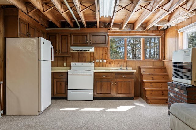 kitchen featuring light carpet, under cabinet range hood, heating unit, white appliances, and wooden walls