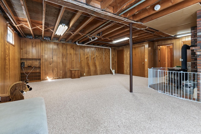 below grade area featuring wooden walls, a wood stove, and carpet