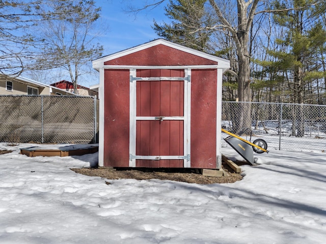 snow covered structure featuring an outbuilding, a storage unit, and fence