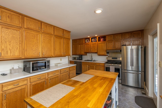 kitchen with brown cabinets, a sink, wood counters, under cabinet range hood, and appliances with stainless steel finishes