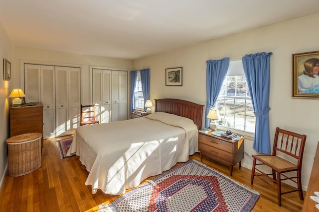 bedroom featuring wood finished floors, baseboards, and two closets