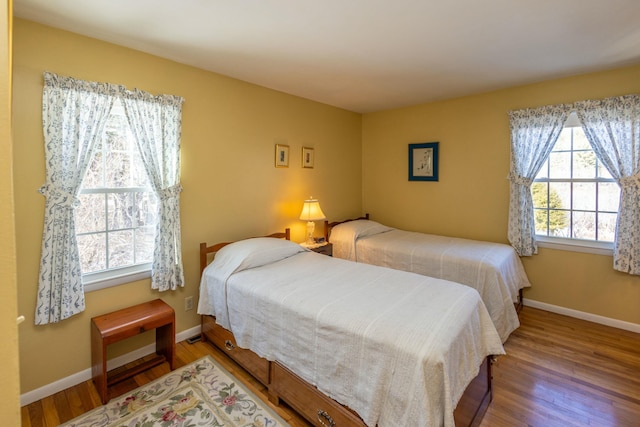 bedroom featuring multiple windows, baseboards, and wood finished floors