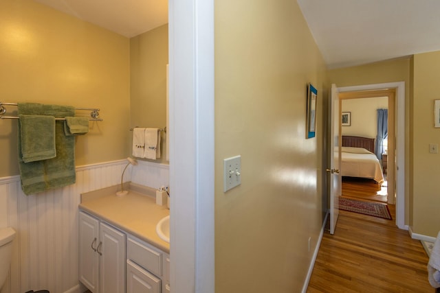 bathroom featuring vanity, toilet, wood finished floors, and wainscoting