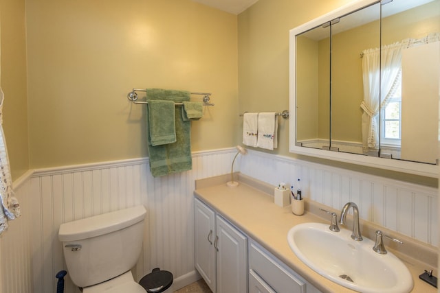 bathroom with vanity, toilet, and a wainscoted wall