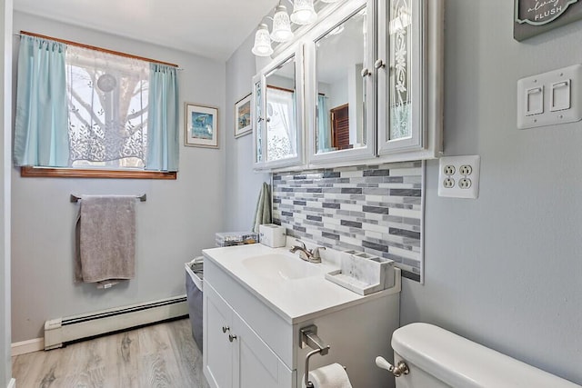 half bath featuring toilet, vanity, wood finished floors, a baseboard radiator, and decorative backsplash