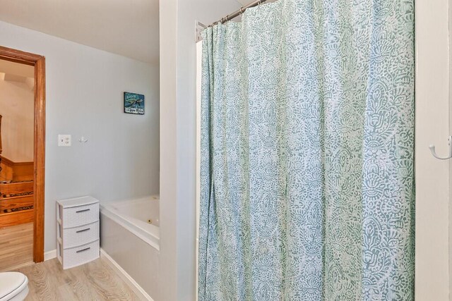 bathroom featuring wood finished floors, toilet, and a bath